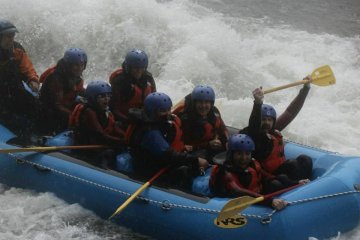 Rafting down Tone River with our champion adventurer holding his paddle up high.