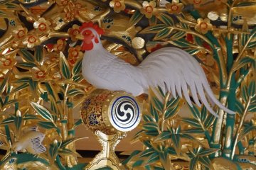 Rooster sits on top of a decorated perch