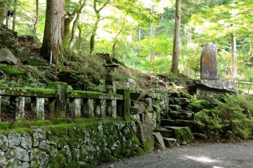 Many markers and small shrines stand among the trees along the path