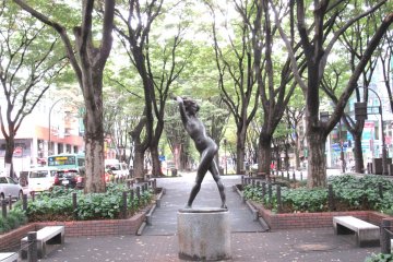 A modern sculpture and tall trees lining Jozenji Dori