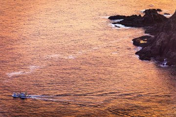 A fishing boat heads out to sea past the rocky cliffs of Kamigoto