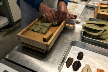 The square-shaped sushi are arranged in a wooden box. 