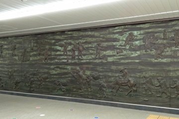A relief of an old artwork showing the "sankin kotai" system. This law of “alternate attendance” forced feudal lords and their samurai and assistants make the long march to Edo (Tokyo) and back regularly. It can be found on the No.2 train platform.