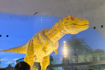 A T-Rex animatronic sits in the middle of an exhibition hall, roaring at the visitors passing by