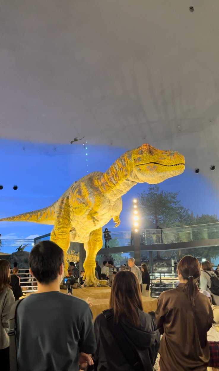 A T-Rex animatronic sits in the middle of an exhibition hall, roaring at the visitors passing by