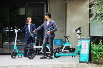 Co-workers chatting next to their LUUP vehicles, holding helmets