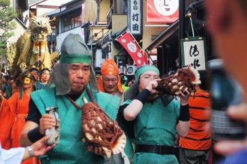The dragon warriors play the traditional horn to attract people around. They lead the group behind with Seiryu-e.